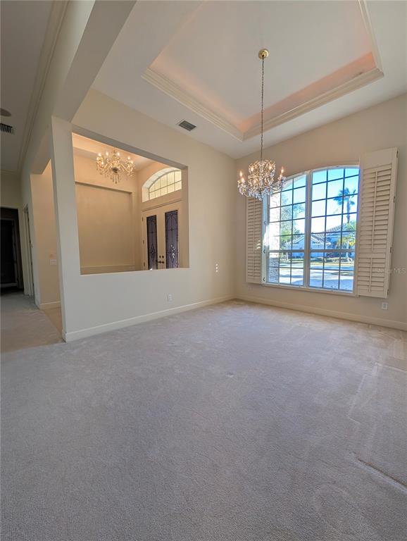 A carpeted dining room features a tray ceiling, crystal chandelier, and a large arched window — 8492 DUNHAM STATION DRIVE, TAMPA, FL