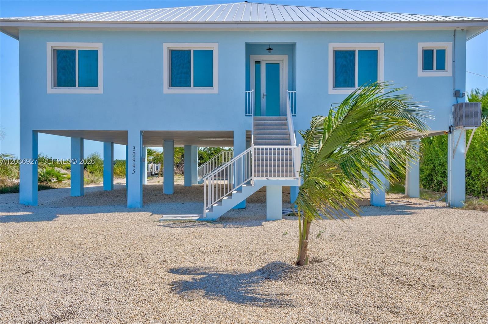 A light blue stilt house stands on a gravel lot with a central staircase — 30995 Watson Blvd, Big Pine FL 33043, BIG PINE, FL