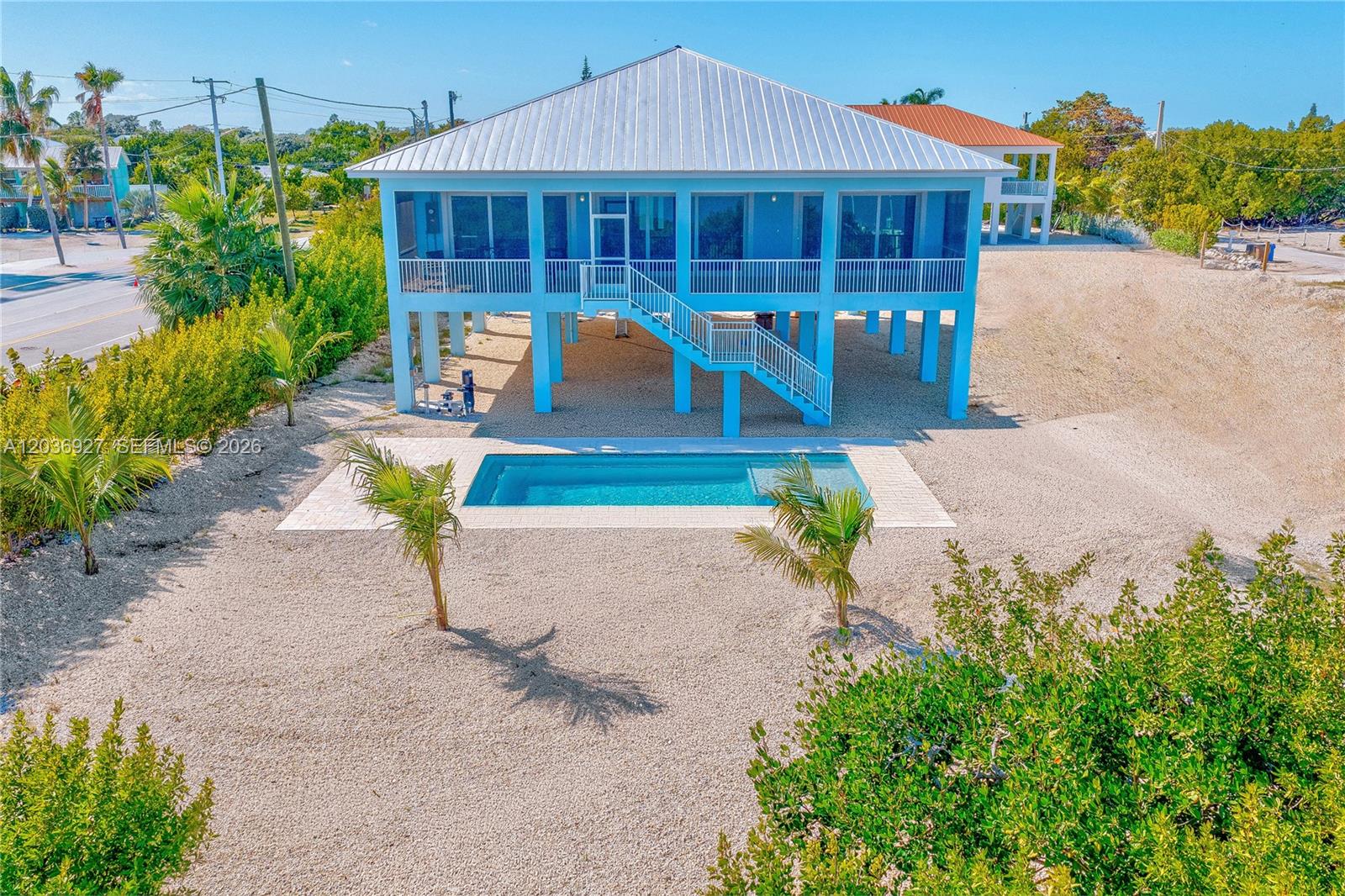 An elevated light blue house with a metal roof features a pool and gravel yard — 30995 Watson Blvd, Big Pine FL 33043, BIG PINE, FL