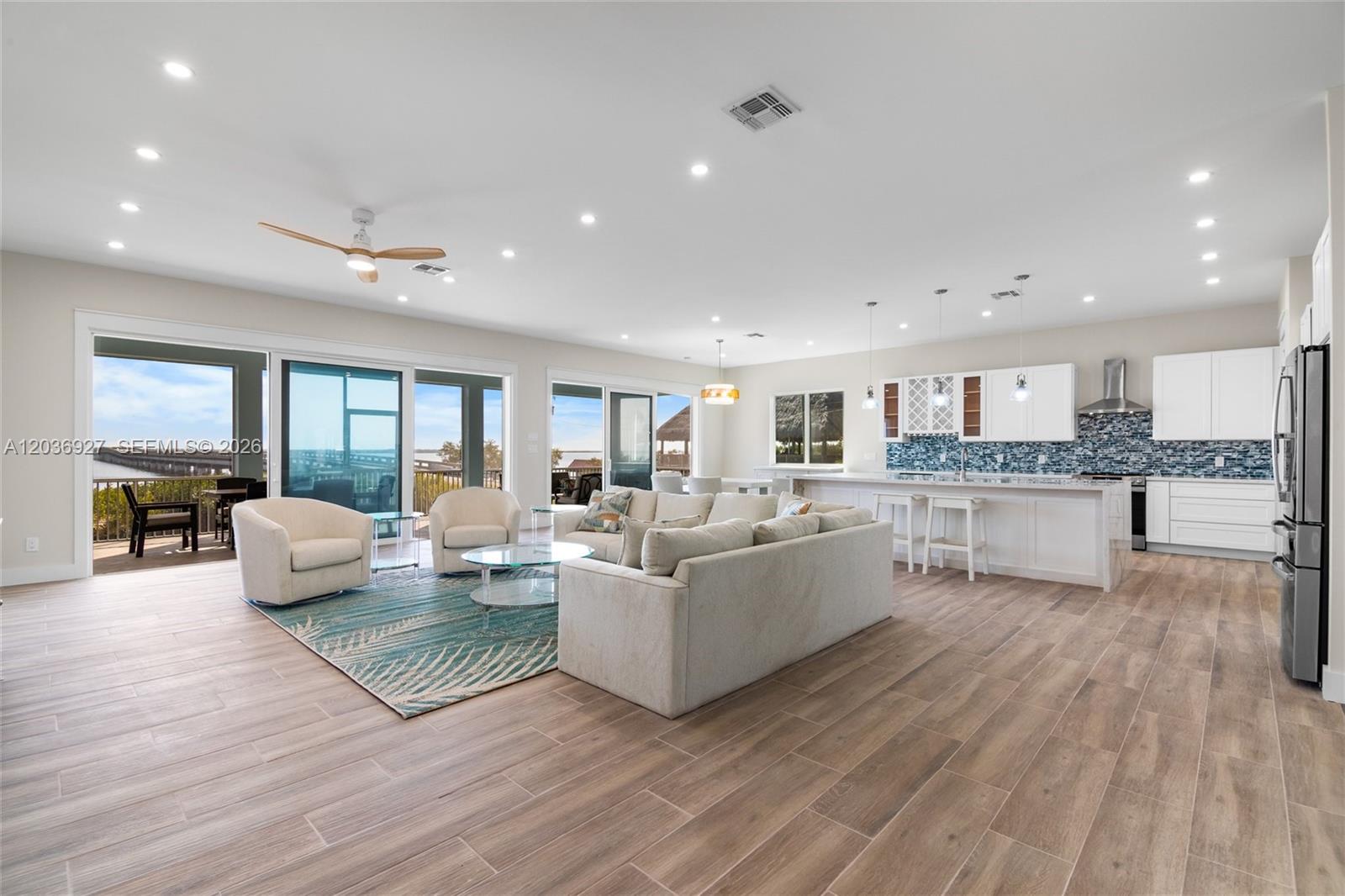 An open-concept living room and kitchen feature light wood-look tile flooring and sliding glass doors — 30995 Watson Blvd, Big Pine FL 33043, BIG PINE, FL