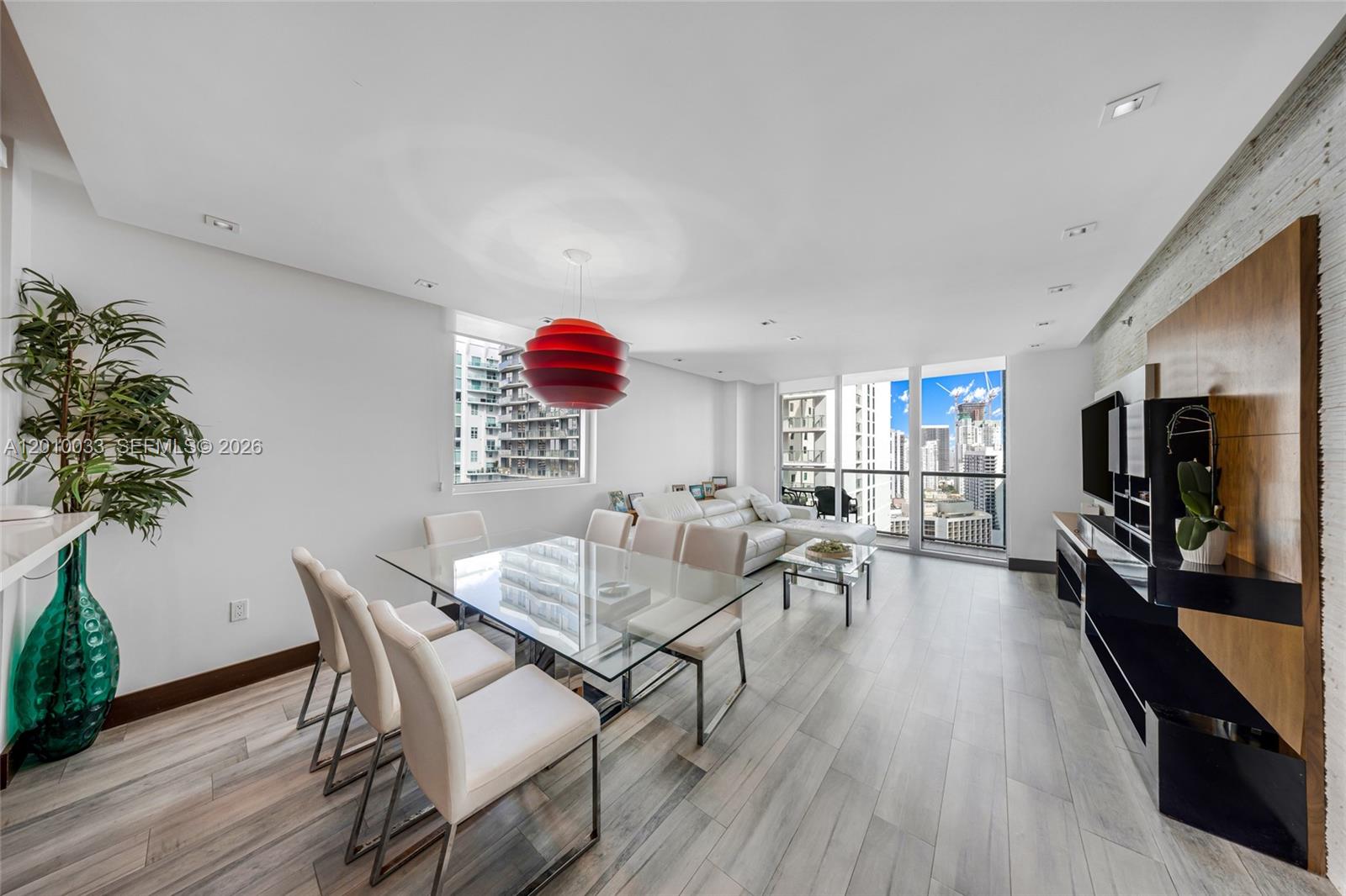 A modern living and dining area features a glass table, white chairs, and city views — 500 Brickell Ave # 3707, Miami FL 33131, MIAMI, FL