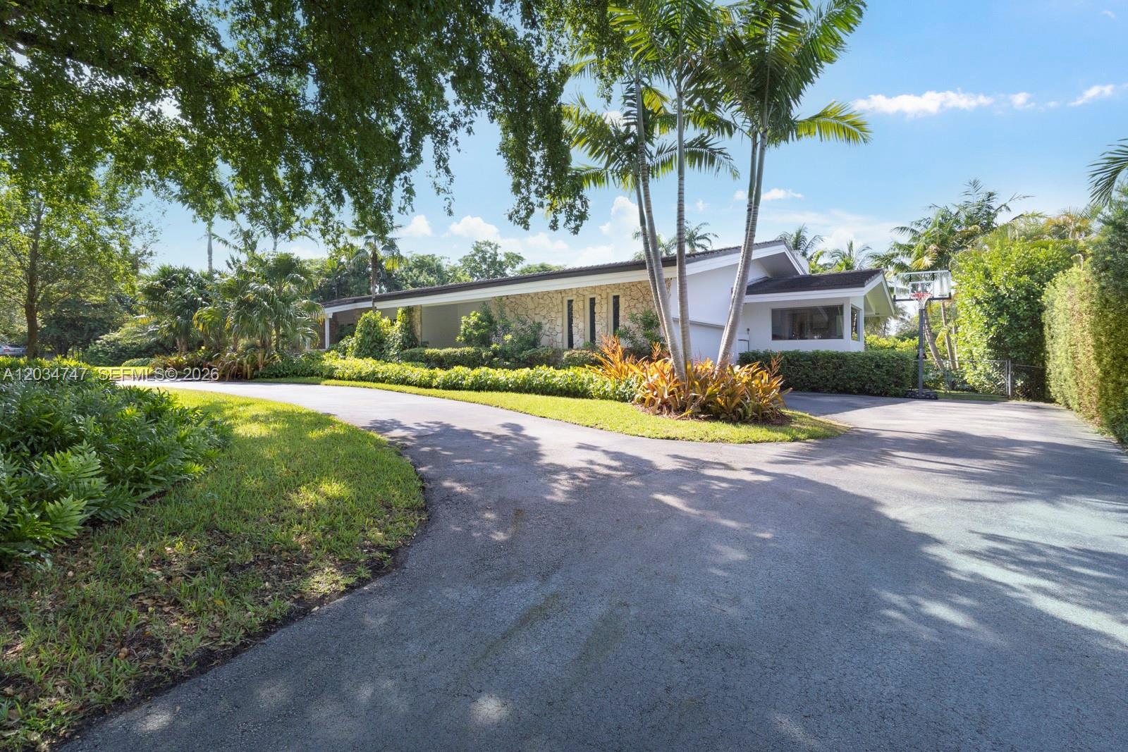 A single-story house with a stone facade and a curved driveway sits among palm trees — 5780 Las Palmas Dr, Coral Gables FL 33156, CORAL GABLES, FL