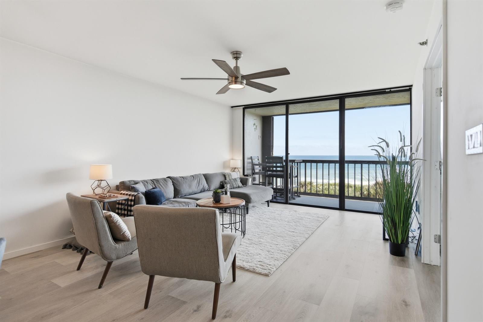 A living room with a gray sectional, two armchairs, and a balcony overlooking the ocean — 8880 S Ocean Drive # 409, Jensen Beach FL 34957, JENSEN BEACH, FL