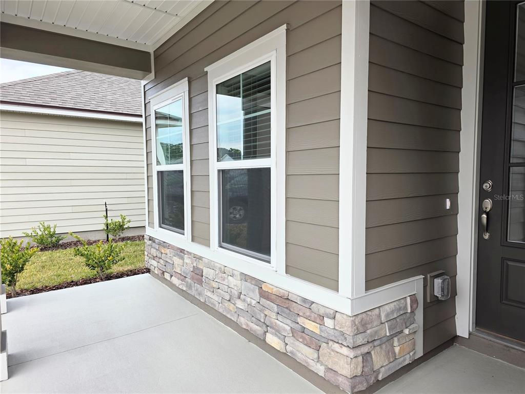 A view of a house exterior featuring tan siding, stone veneer, and two windows — 3295 WILLOWLEAF LANE, GREEN COVE SPRINGS, FL