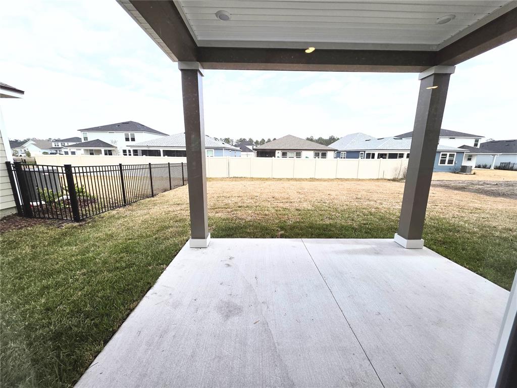 A concrete patio with two support columns overlooks a fenced backyard and neighboring houses — 3295 WILLOWLEAF LANE, GREEN COVE SPRINGS, FL