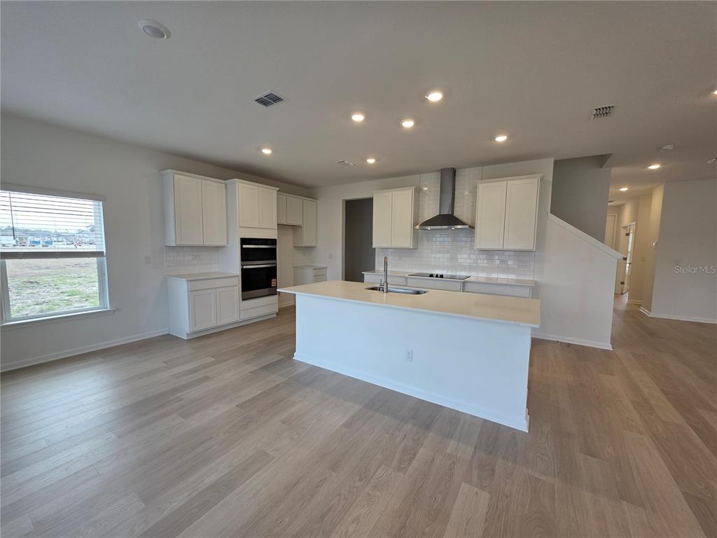 A kitchen features white cabinets, a central island, stainless steel appliances, and light wood flooring — 3295 WILLOWLEAF LANE, GREEN COVE SPRINGS, FL