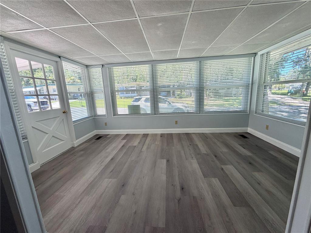 A sunroom features gray wood-look flooring, a drop ceiling, and multiple windows with blinds — 103 ROYAL PALM DRIVE, LEESBURG, FL