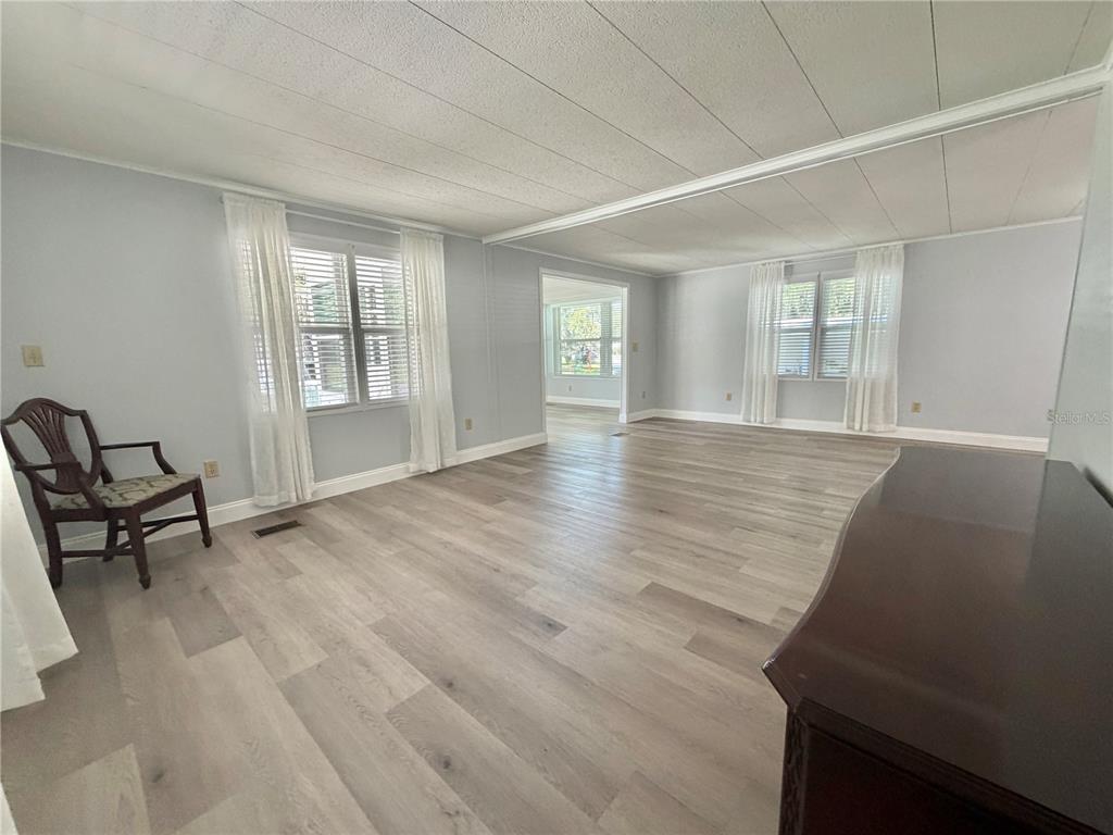 A spacious living room features light wood-look flooring, white walls, and large windows with curtains — 103 ROYAL PALM DRIVE, LEESBURG, FL