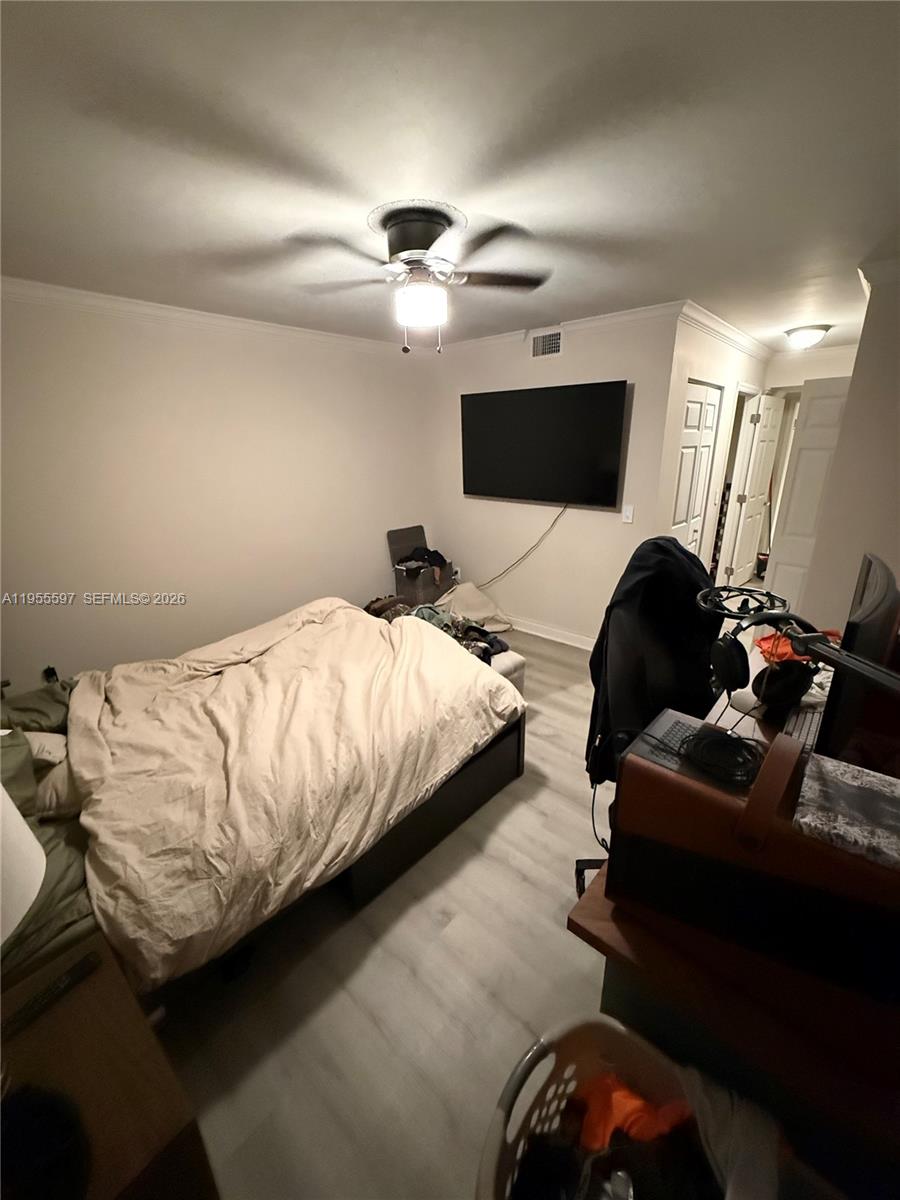 A bedroom features a bed, a wall-mounted television, and light-colored wood-look flooring — 7765 SW 86th St # 112, Miami FL 33143, MIAMI, FL