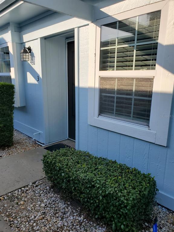 A light blue exterior wall features a front door, a window, and a small hedge — 11135 CARRIAGE HILL DRIVE UNIT 3, PORT RICHEY, FL