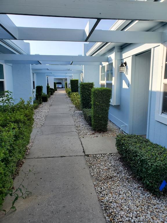 A concrete walkway leads between two light blue buildings with a wooden pergola overhead — 11135 CARRIAGE HILL DRIVE UNIT 3, PORT RICHEY, FL