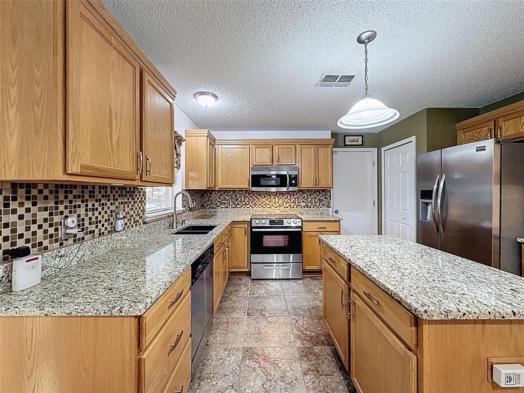 A kitchen features oak cabinets, granite countertops, stainless steel appliances, and a central island — 3181 DELTONA BOULEVARD, SPRING HILL, FL