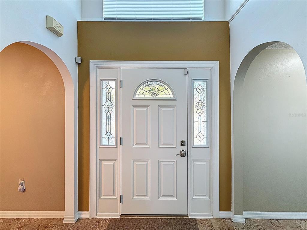 A white front door with glass sidelights is centered between two arched wall openings — 3181 DELTONA BOULEVARD, SPRING HILL, FL
