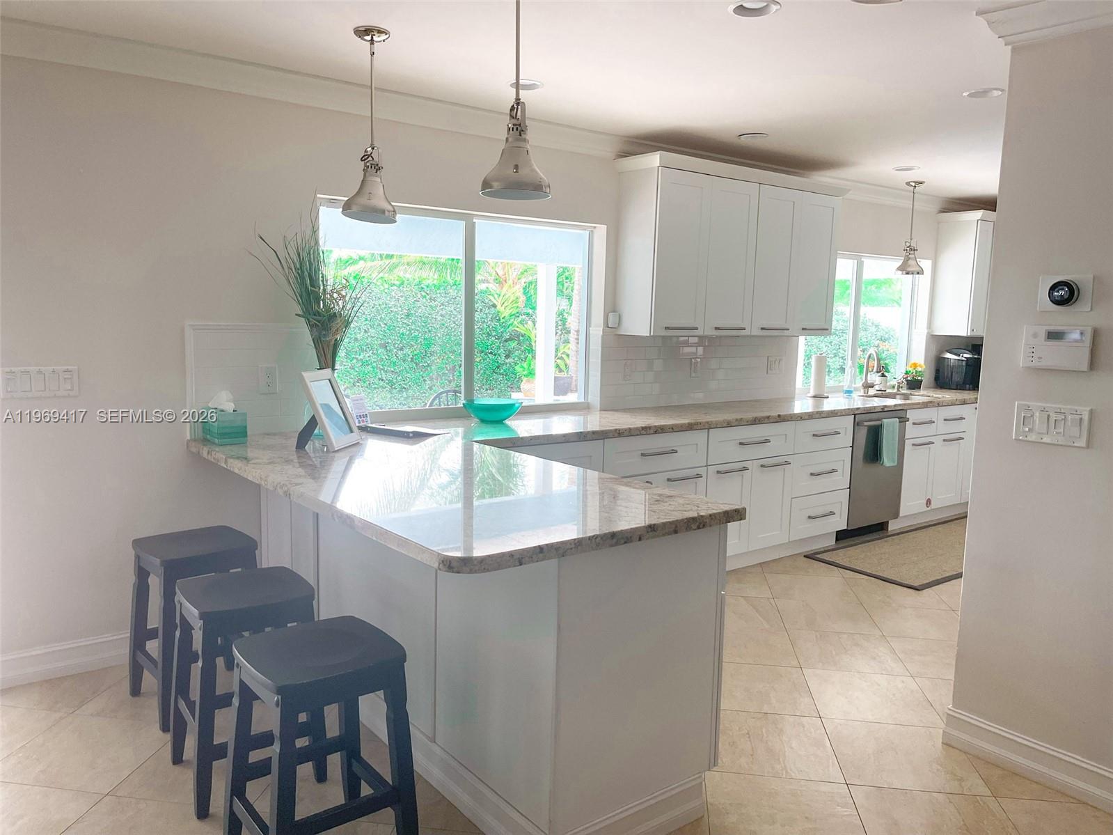 A kitchen features white cabinets, granite countertops, a breakfast bar with stools, and tile flooring — 2932 NE 36th St, Lighthouse Point FL 33064, LIGHTHOUSE POINT, FL