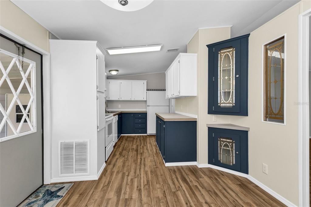 A kitchen features white upper cabinets, dark blue lower cabinets, and wood-look flooring — 503 MADONNA, NORTH PORT, FL
