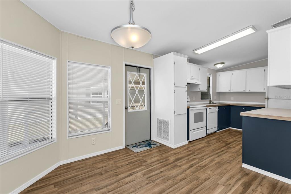 A kitchen and dining area with white cabinets, blue lower cabinets, and wood-look flooring — 503 MADONNA, NORTH PORT, FL