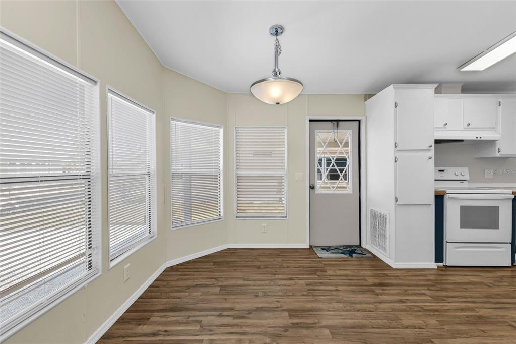 A dining area with wood-look flooring, large windows, a pendant light, and an adjacent kitchen — 503 MADONNA, NORTH PORT, FL