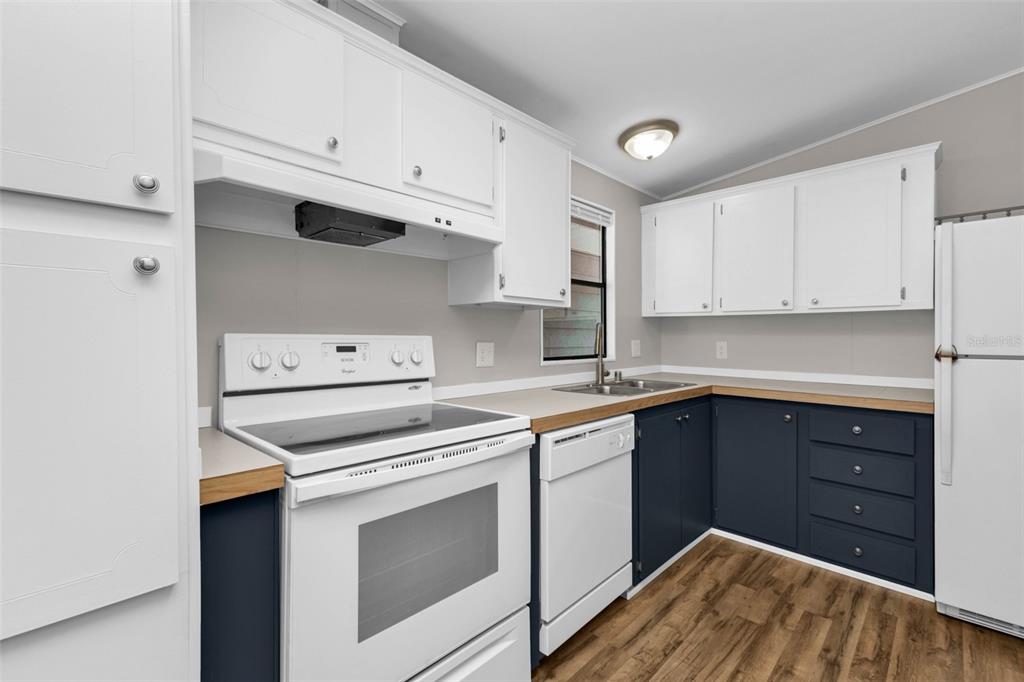 A kitchen features white upper cabinets, dark blue lower cabinets, and white appliances — 503 MADONNA, NORTH PORT, FL