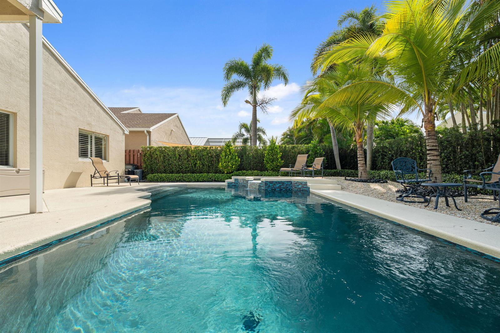 A swimming pool with a tiled spillover spa sits on a patio beside a house — 4620 SE Winter Haven Court, Stuart FL 34997, STUART, FL