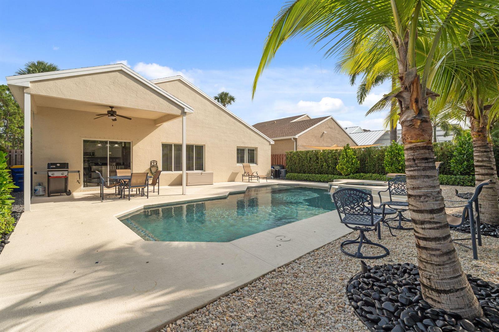 A backyard features a swimming pool, a covered patio, and palm trees on a sunny day — 4620 SE Winter Haven Court, Stuart FL 34997, STUART, FL