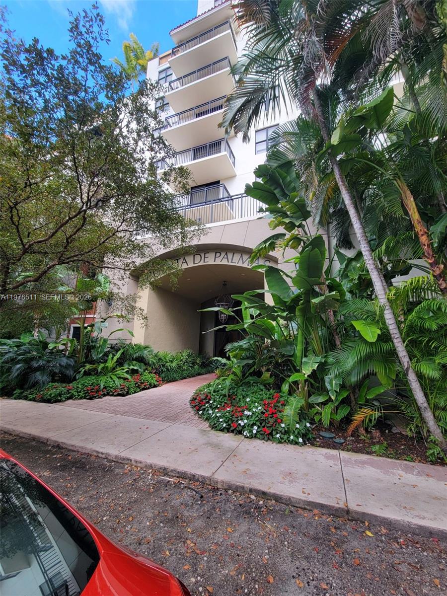 A multi-story residential building entrance features a stone archway, balconies, and lush tropical landscaping — 888 S Douglas Rd # 1110, Coral Gables FL 33134, CORAL GABLES, FL