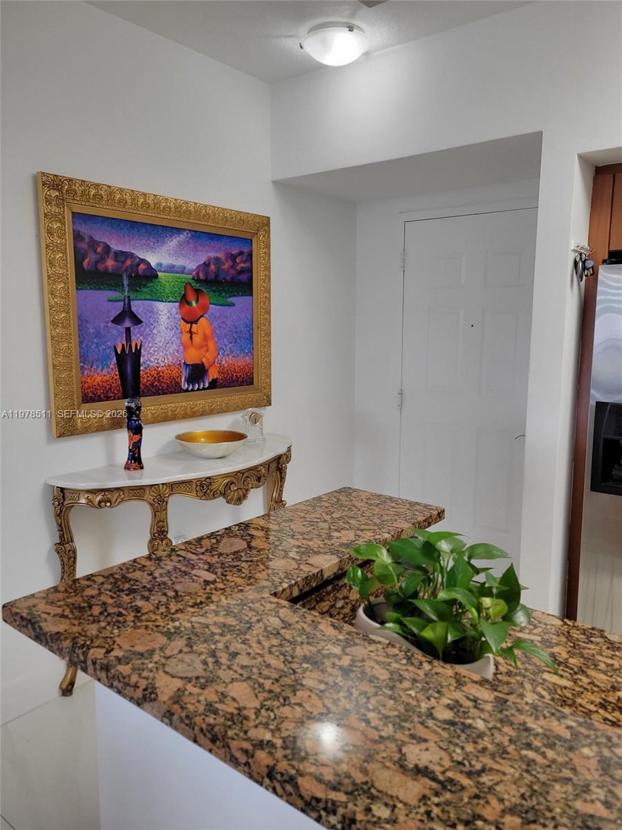 A kitchen counter with granite countertops sits in front of a console table and painting — 888 S Douglas Rd # 1110, Coral Gables FL 33134, CORAL GABLES, FL