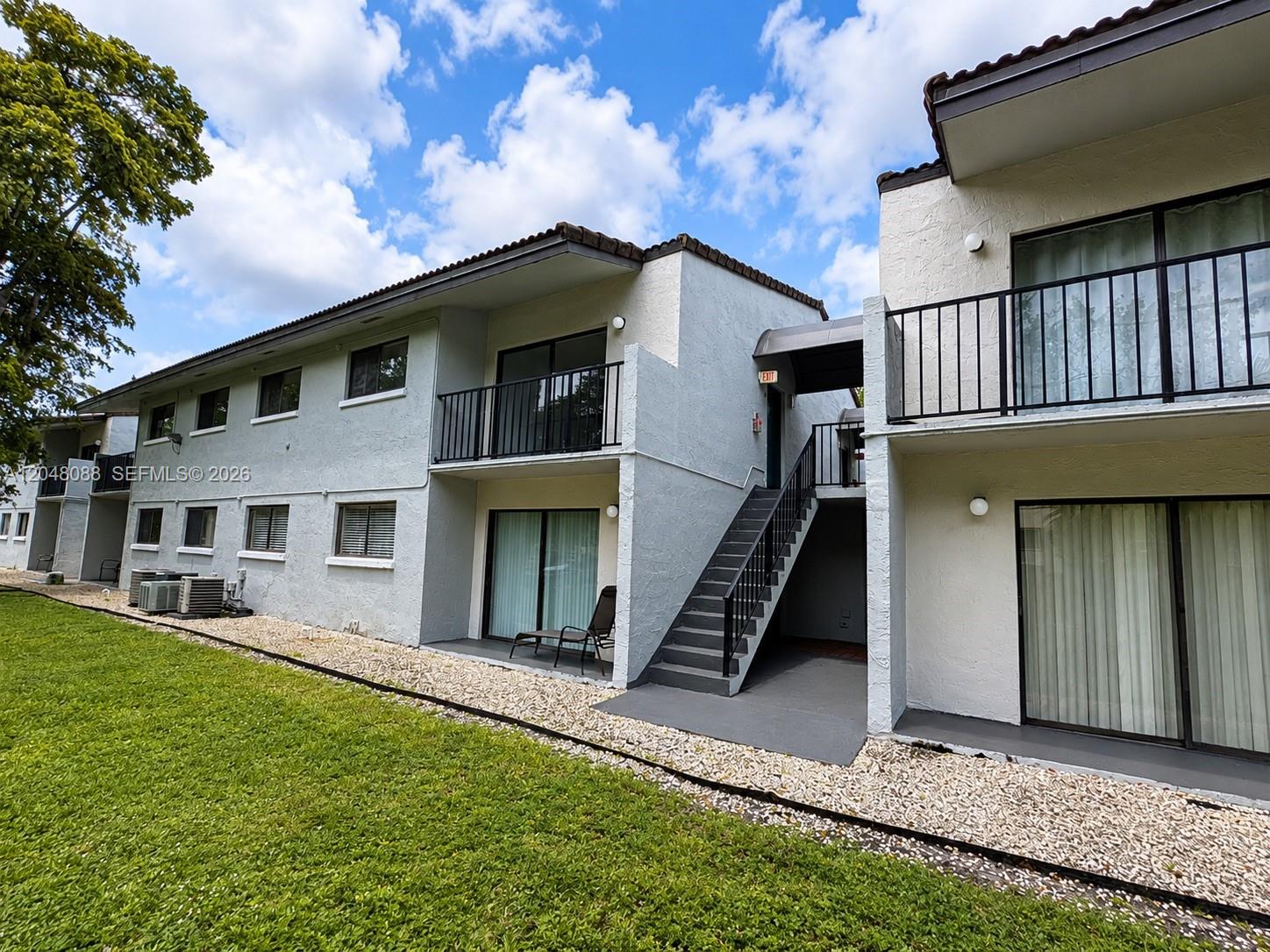 The exterior of a two-story apartment building features white stucco walls and metal staircases — 7095 NW 179th St # 209, Hialeah FL 33015, HIALEAH, FL