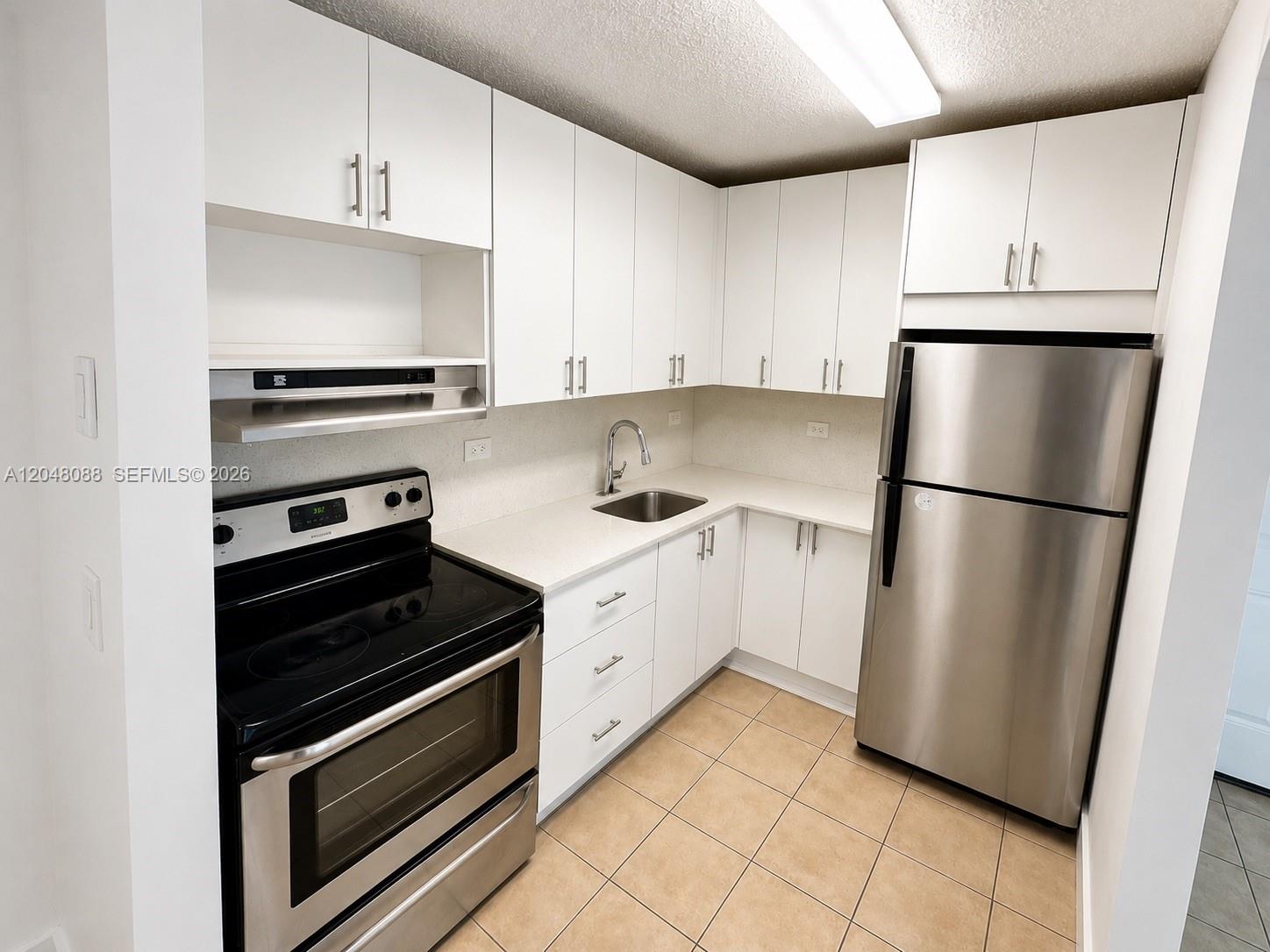 A kitchen features white cabinets, stainless steel appliances, light countertops, and tan tile flooring — 7095 NW 179th St # 209, Hialeah FL 33015, HIALEAH, FL