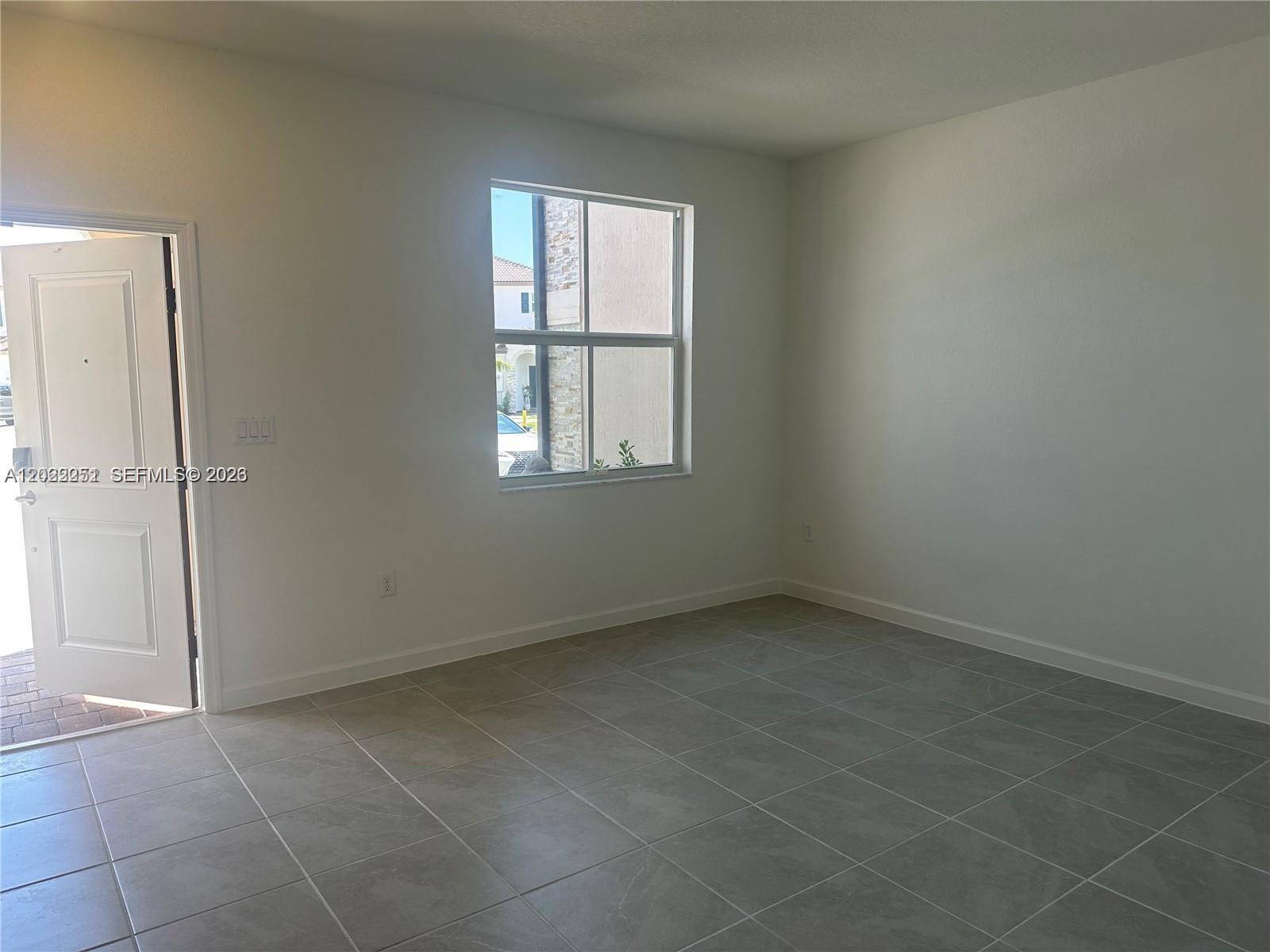 An empty room features white walls, gray tile flooring, and a window overlooking a street — 12210 NW 23rd Path # 0, Miami FL 33167, MIAMI, FL