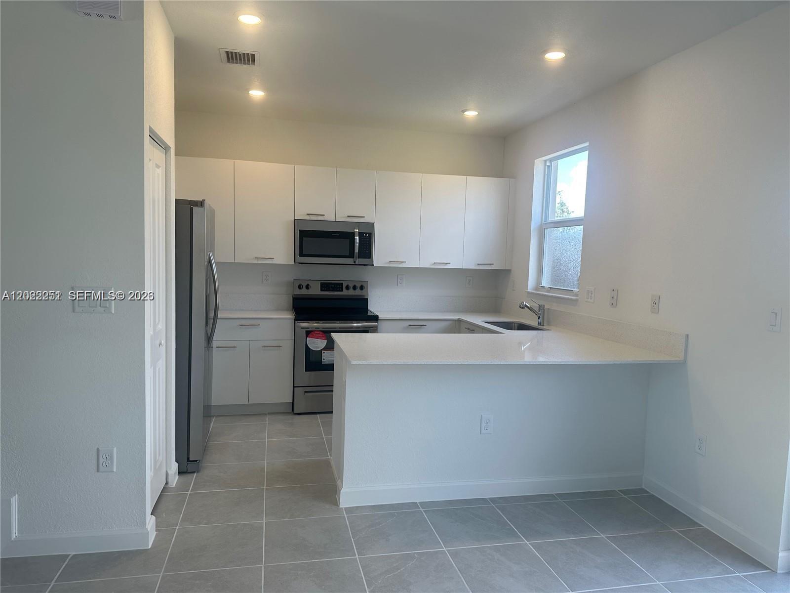 A modern kitchen features white cabinets, stainless steel appliances, and a peninsula with quartz countertops — 12210 NW 23rd Path # 0, Miami FL 33167, MIAMI, FL