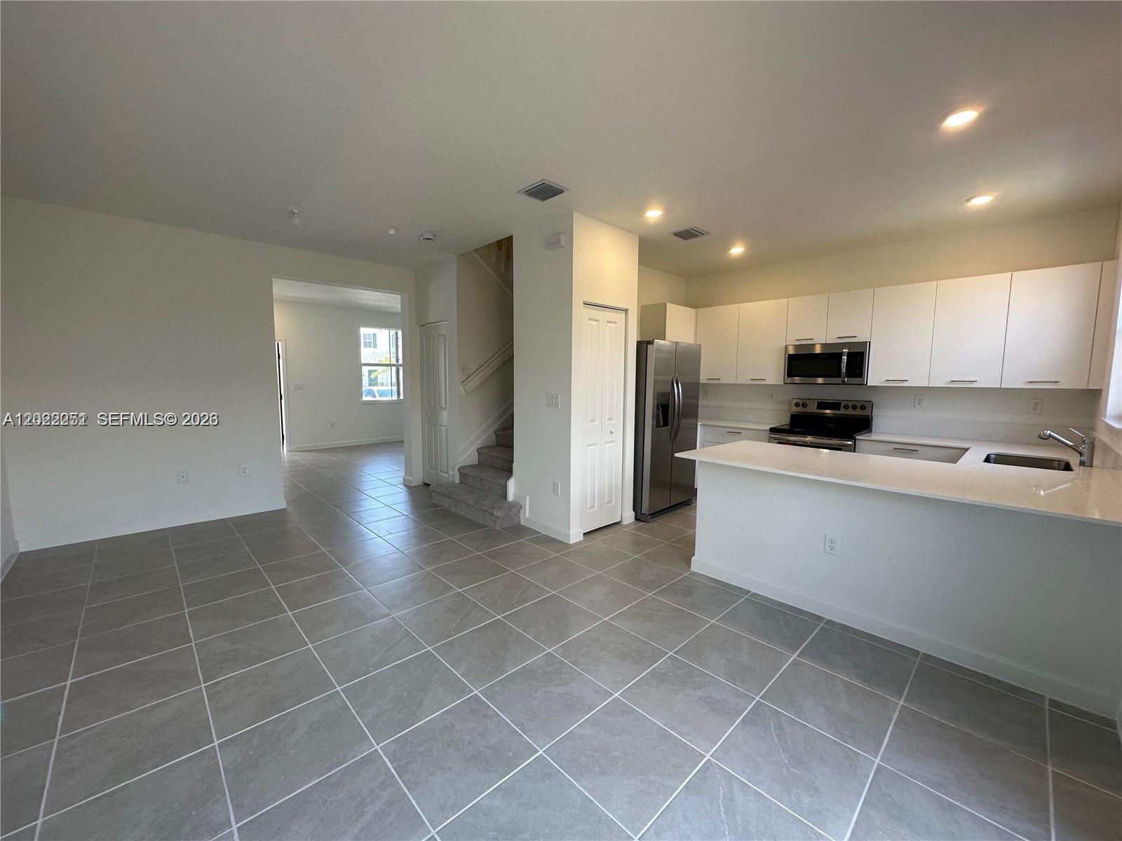 A kitchen with white cabinets and a breakfast bar overlooks a tiled living area — 12210 NW 23rd Path # 0, Miami FL 33167, MIAMI, FL