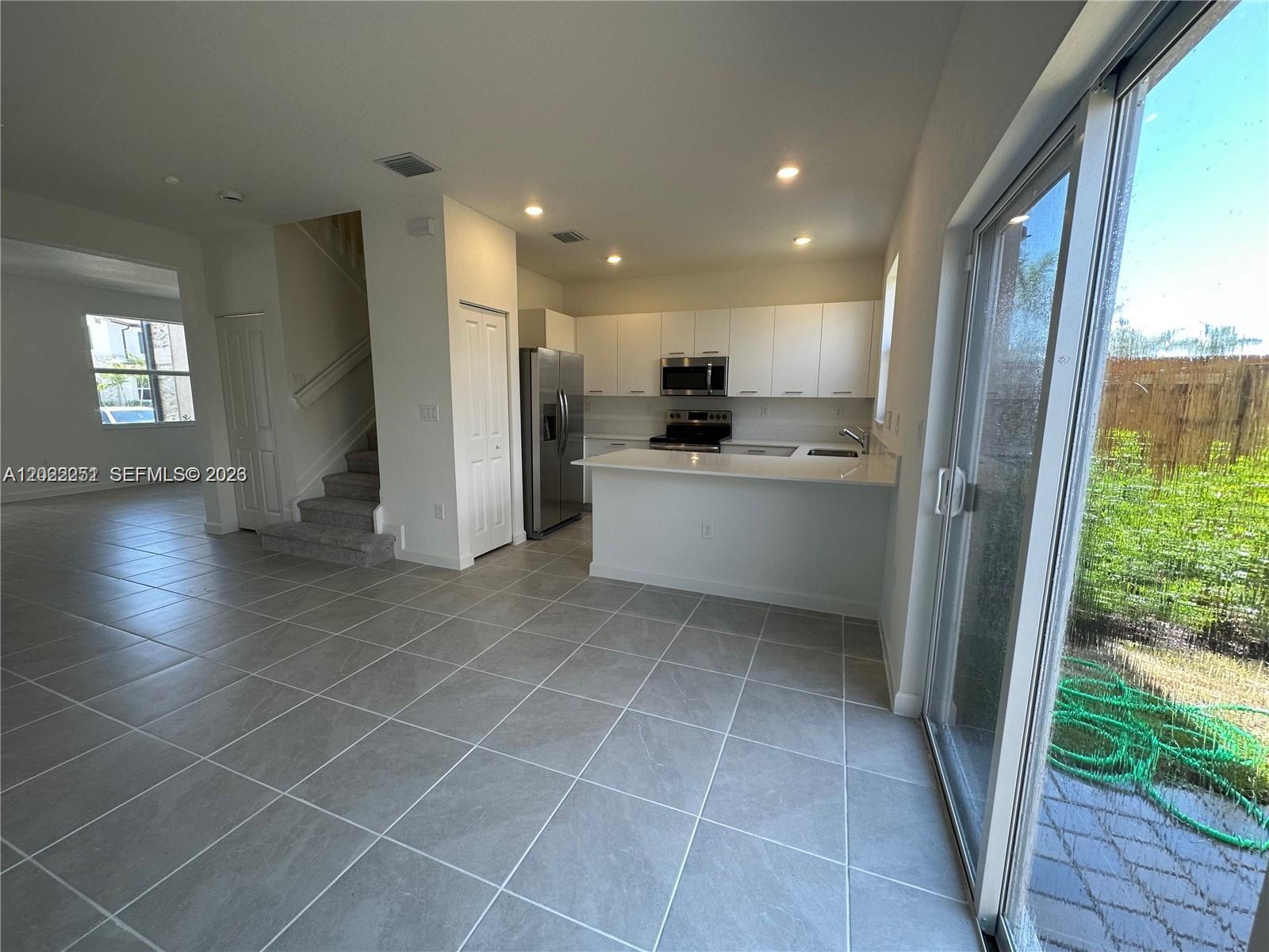 A kitchen with white cabinets and a breakfast bar opens to a tiled living area — 12210 NW 23rd Path # 0, Miami FL 33167, MIAMI, FL