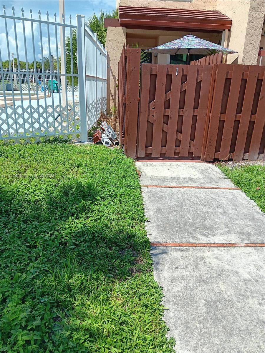 A concrete walkway leads to a wooden gate and a patio area with an umbrella — 271 W Park Dr # 7, Miami FL 33172, MIAMI, FL