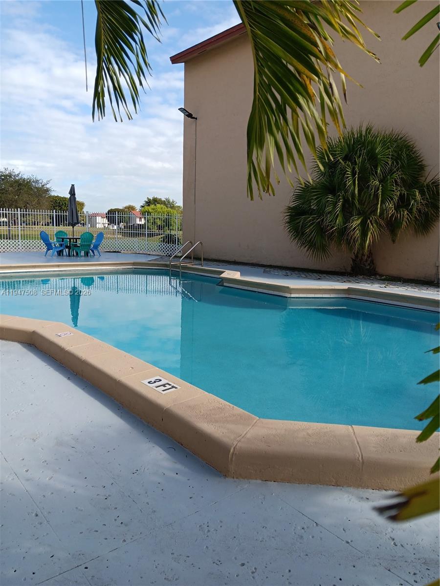 A swimming pool with a shallow end and patio furniture sits beside a tan building — 271 W Park Dr # 7, Miami FL 33172, MIAMI, FL