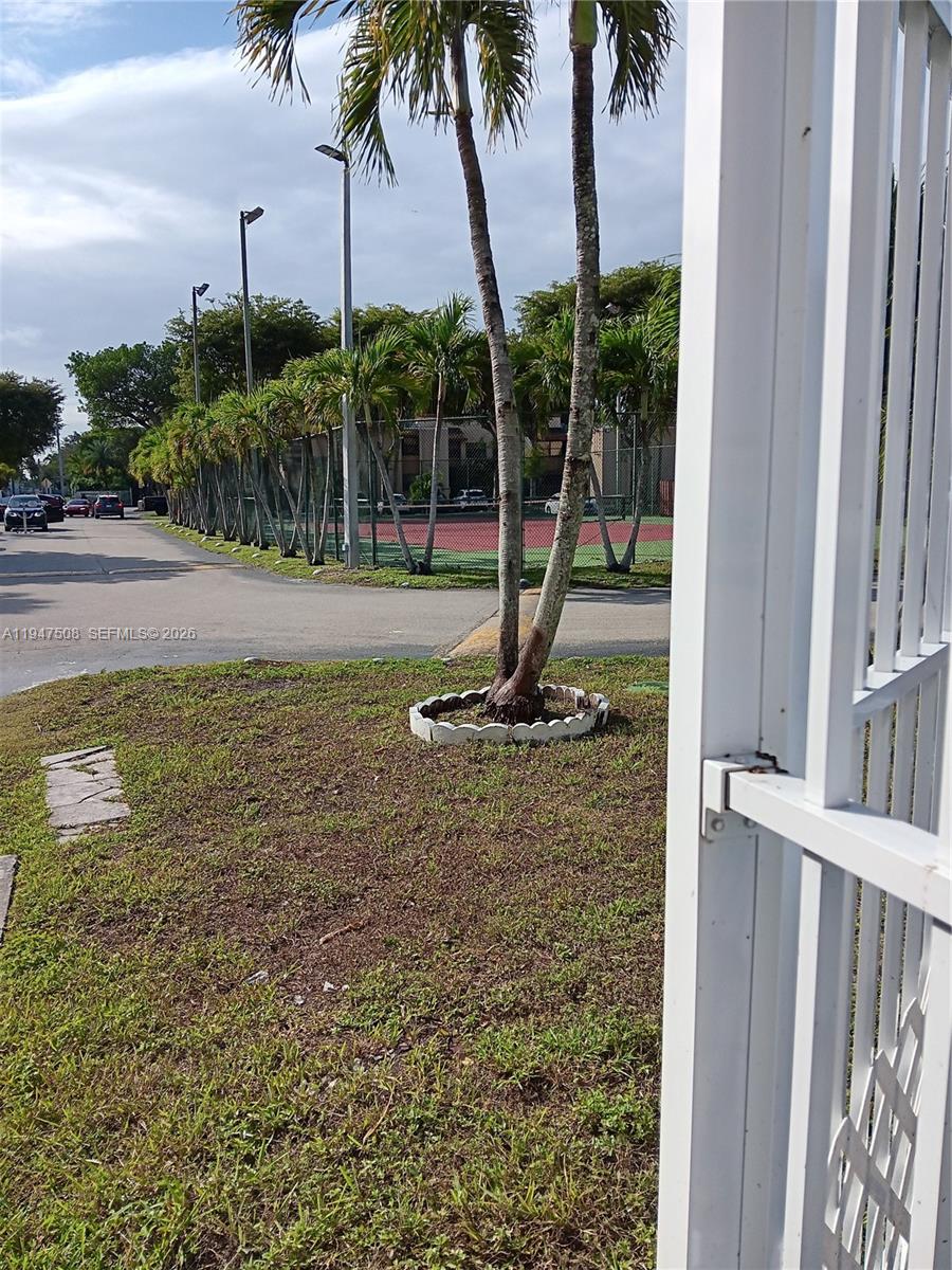 A white metal gate stands in the foreground next to palm trees and a tennis court — 271 W Park Dr # 7, Miami FL 33172, MIAMI, FL