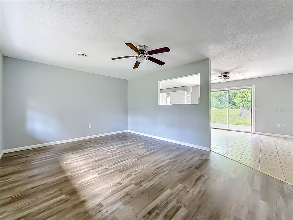 An empty room with wood-look flooring, a ceiling fan, and a pass-through window to a sunroom — 3309 NE 16TH AVENUE, OCALA, FL