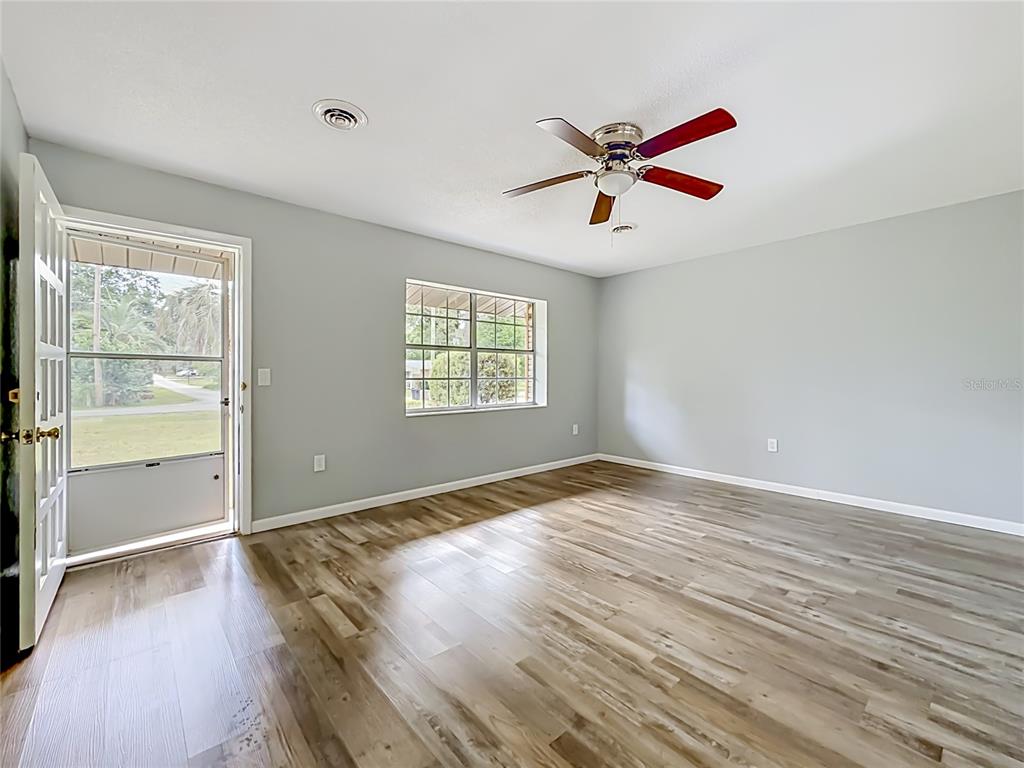 An empty room features light gray walls, wood-look flooring, a ceiling fan, and an exterior door — 3309 NE 16TH AVENUE, OCALA, FL