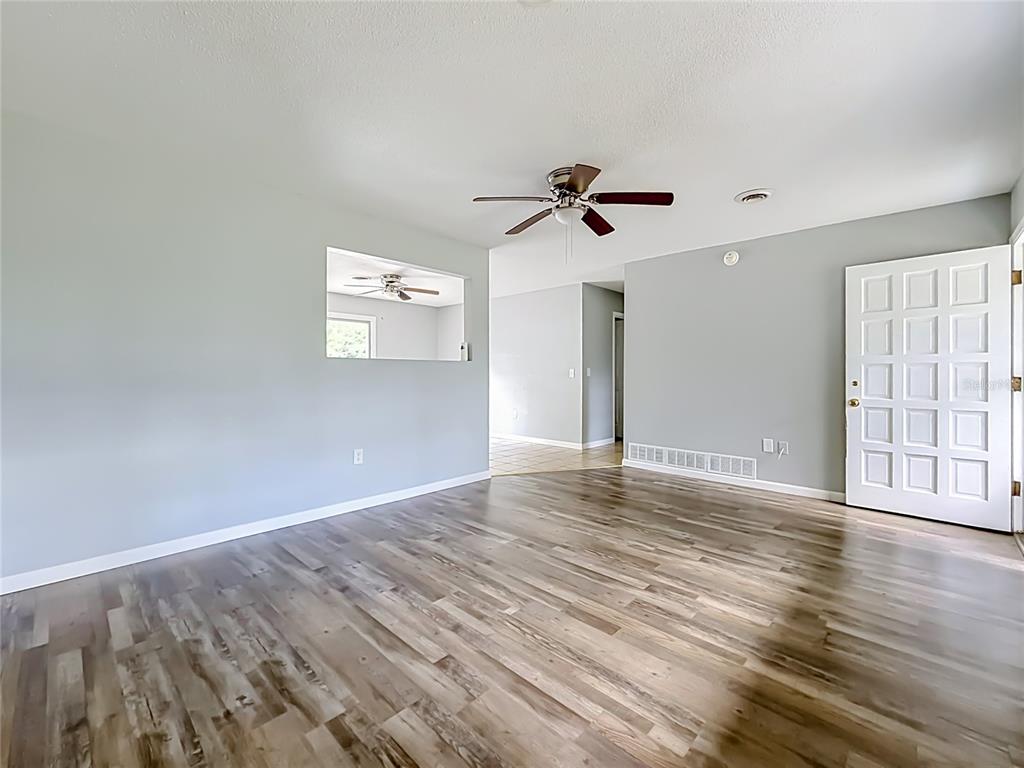An empty living room features light gray walls, wood-look flooring, a ceiling fan, and a pass-through — 3309 NE 16TH AVENUE, OCALA, FL