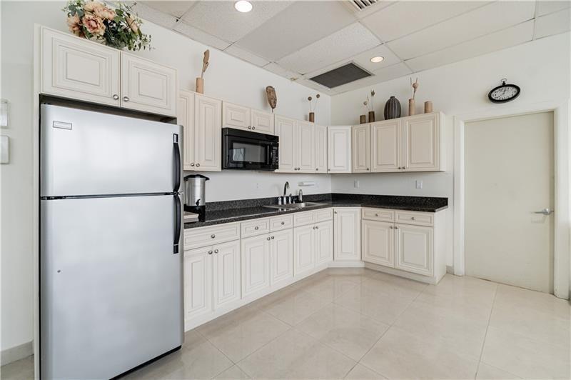 A kitchen features cream-colored cabinets, dark granite countertops, a stainless steel refrigerator, and tiled floors — 521 N Riverside Drive # 602, Pompano Beach FL 33062, POMPANO BEACH, FL