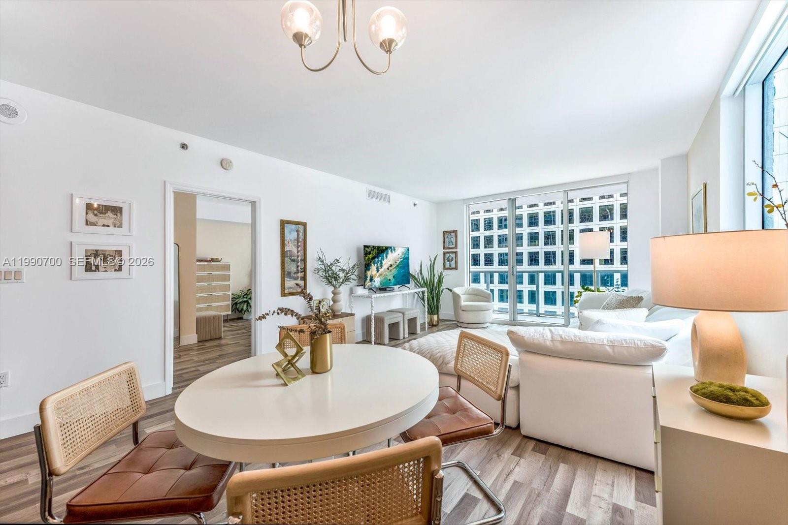 A bright living and dining area features white walls, wood-look flooring, and large floor-to-ceiling windows — 500 Brickell Ave # 1810, Miami FL 33131, MIAMI, FL