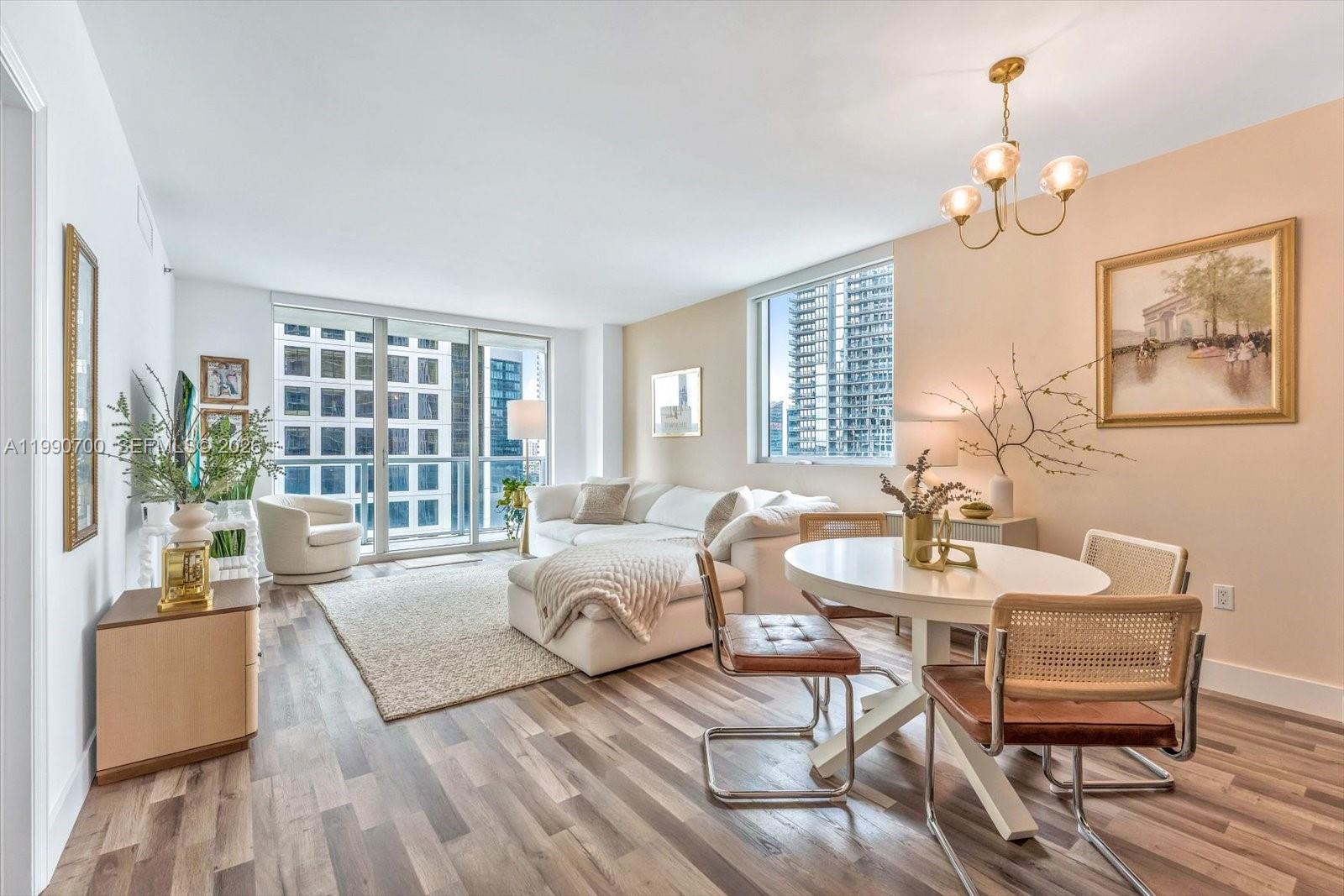 A bright living and dining area features wood-look flooring, a white sectional, and floor-to-ceiling windows — 500 Brickell Ave # 1810, Miami FL 33131, MIAMI, FL