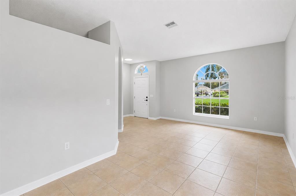 An empty living room features light gray walls, tan tile flooring, and an arched window — 9917 SHADOW CREEK DRIVE, ORLANDO, FL