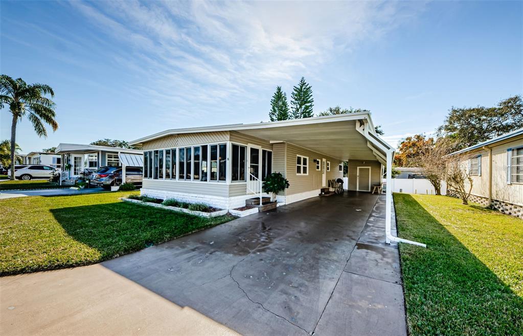 A single-story manufactured home features a large attached carport and a glass-enclosed front porch — 39820 US HIGHWAY 19 N UNIT 15, TARPON SPRINGS, FL