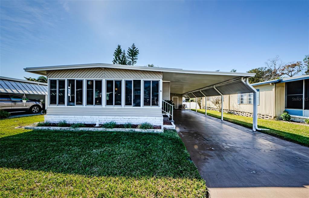 A single-story manufactured home with a large front window, white brick base, and attached carport — 39820 US HIGHWAY 19 N UNIT 15, TARPON SPRINGS, FL