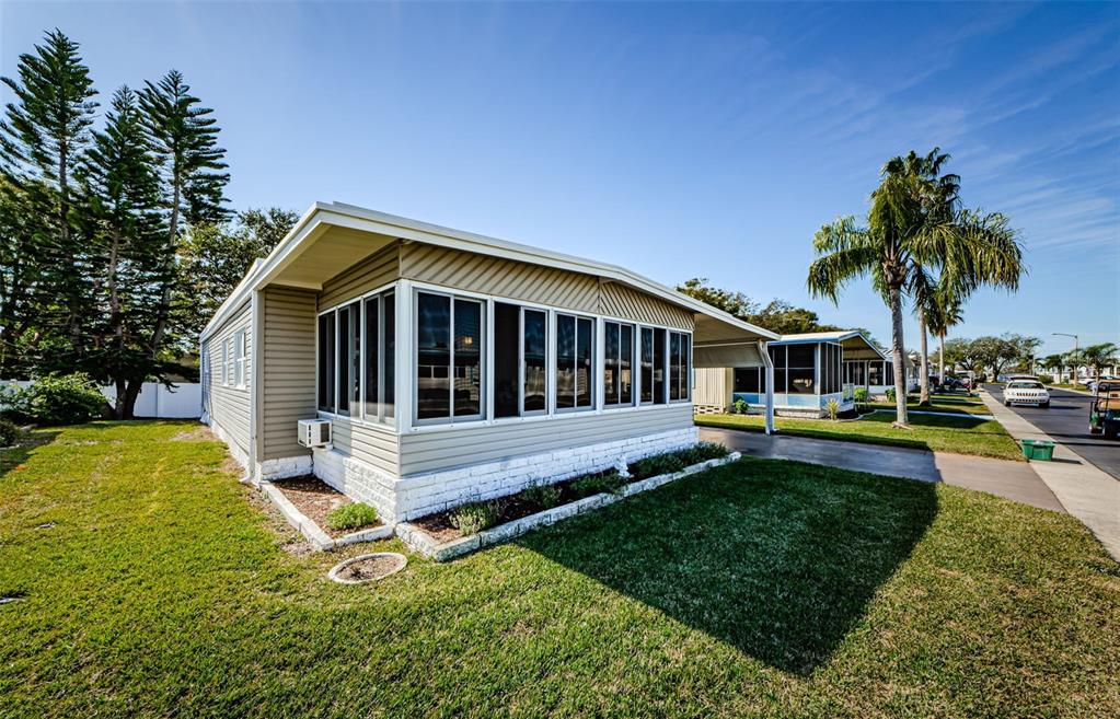 A single-story manufactured home with a screened-in porch, white brick base, and attached carport — 39820 US HIGHWAY 19 N UNIT 15, TARPON SPRINGS, FL