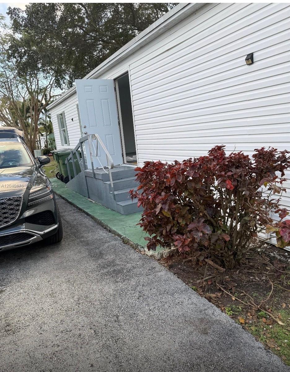 A white mobile home exterior features a set of gray stairs leading to an open door — 100 NE 6th Ave # 504, Homestead FL 33030, HOMESTEAD, FL