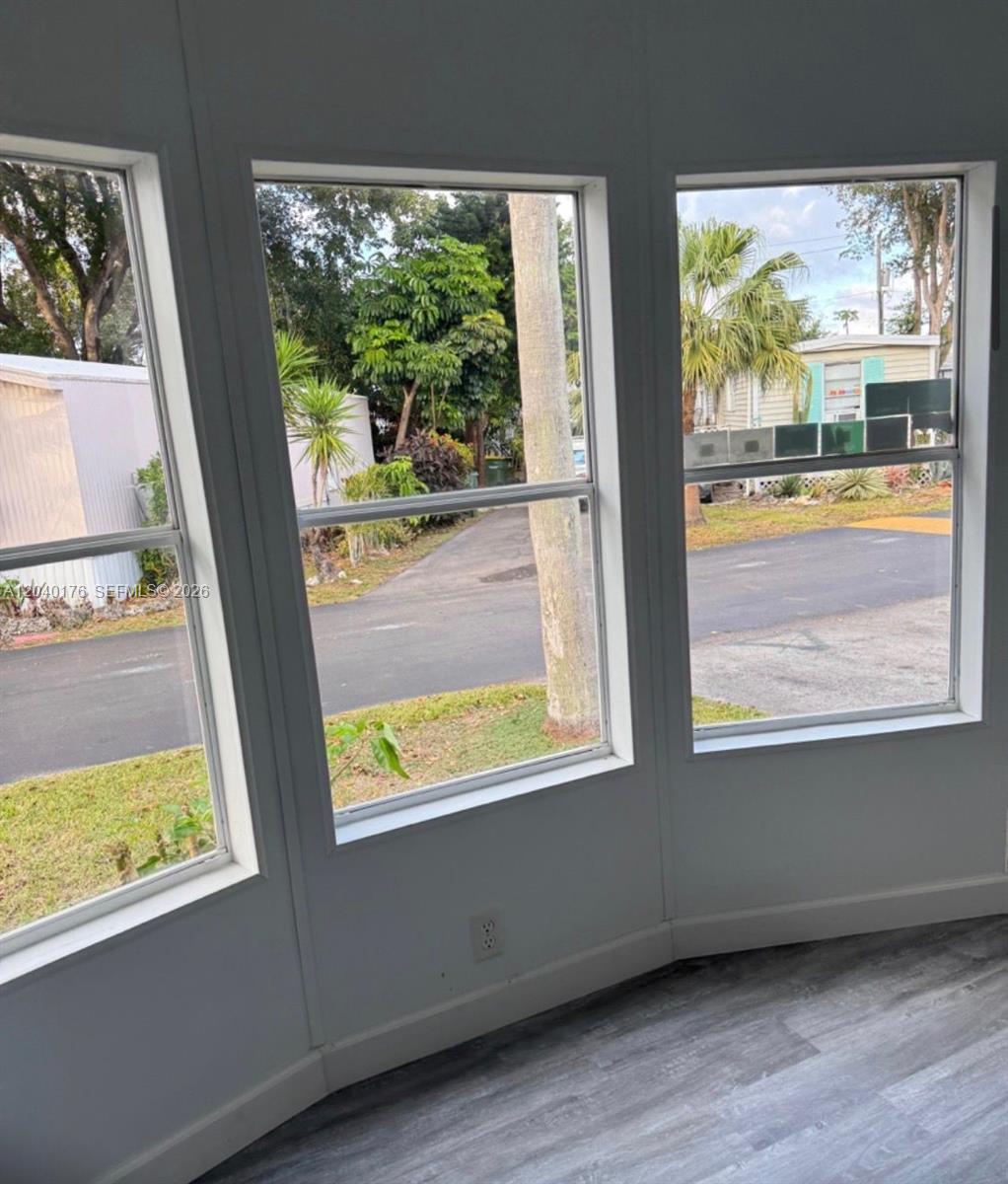 A room with gray wood-look flooring features a bay window overlooking a neighborhood street — 100 NE 6th Ave # 504, Homestead FL 33030, HOMESTEAD, FL