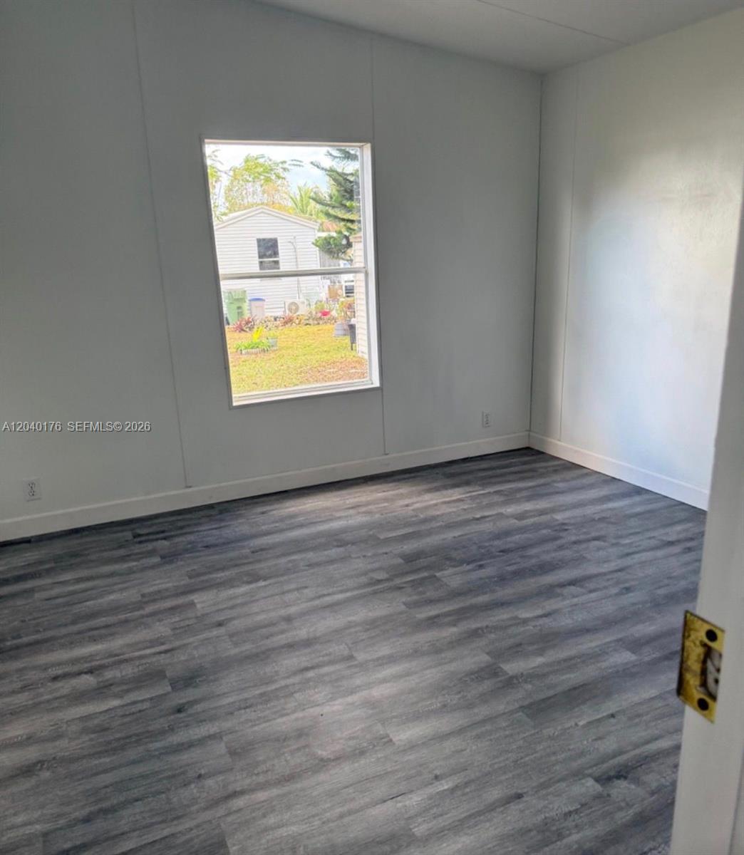 An empty room features white walls, gray wood-look flooring, and a window overlooking a yard — 100 NE 6th Ave # 504, Homestead FL 33030, HOMESTEAD, FL
