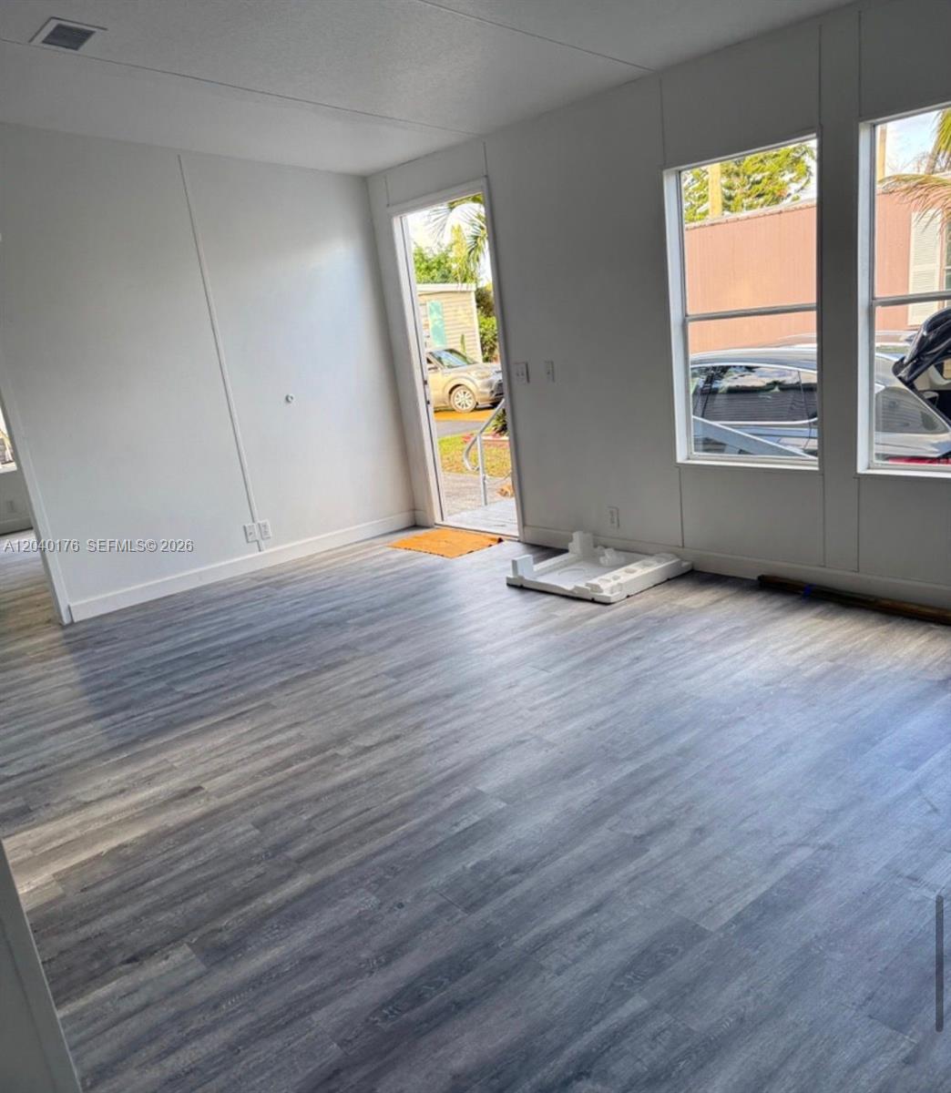An empty room features gray wood-look flooring, white walls, and a door leading outside — 100 NE 6th Ave # 504, Homestead FL 33030, HOMESTEAD, FL