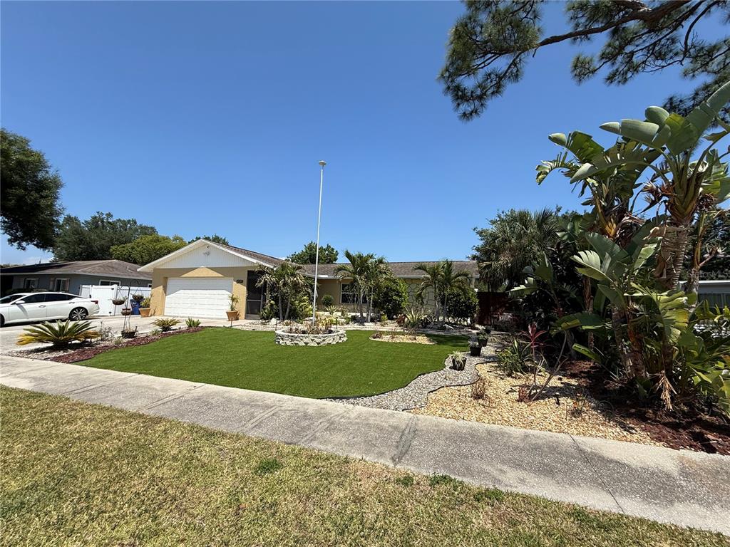 A single-story house with a white garage, artificial turf lawn, and tropical landscaping — 2729 NODOSA DRIVE, SARASOTA, FL